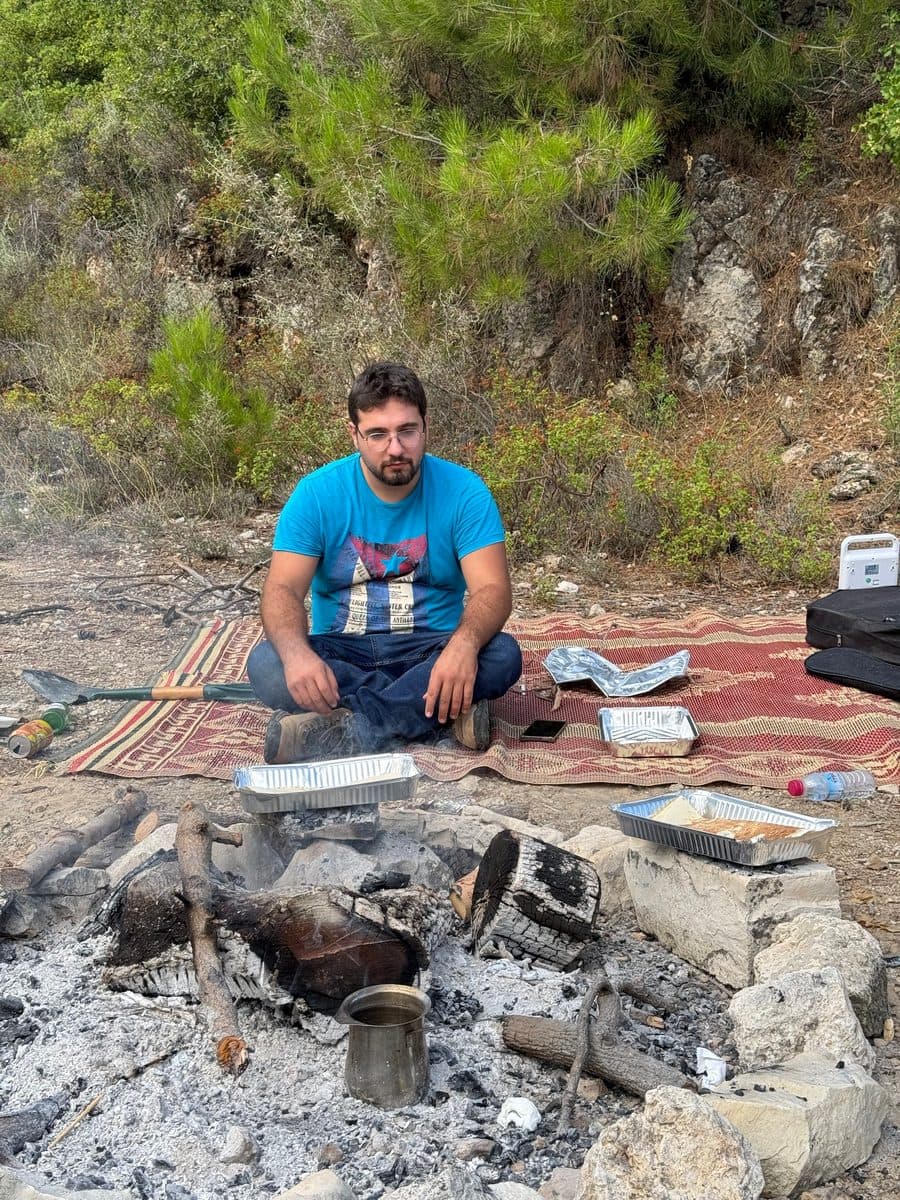 Patrick sitting cross-legged by a campfire, staring at the ashes